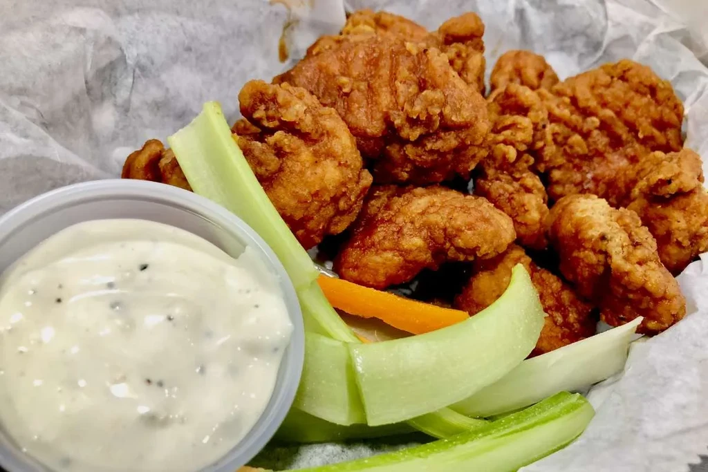 Fried chicken pieces, creamy sauce, celery, and carrots in a basket.