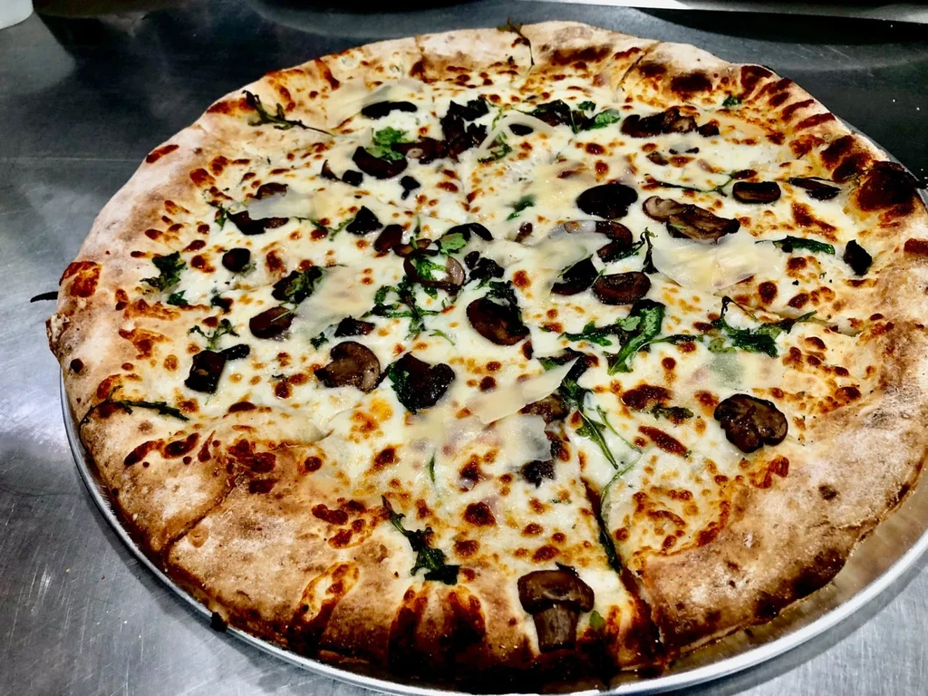 Pre-sliced artisanal pizza with mushrooms, herbs, and parmesan on a silver pan.