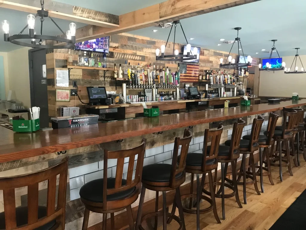 Rustic bar with a long wooden counter, stools, liquor, and beer taps.