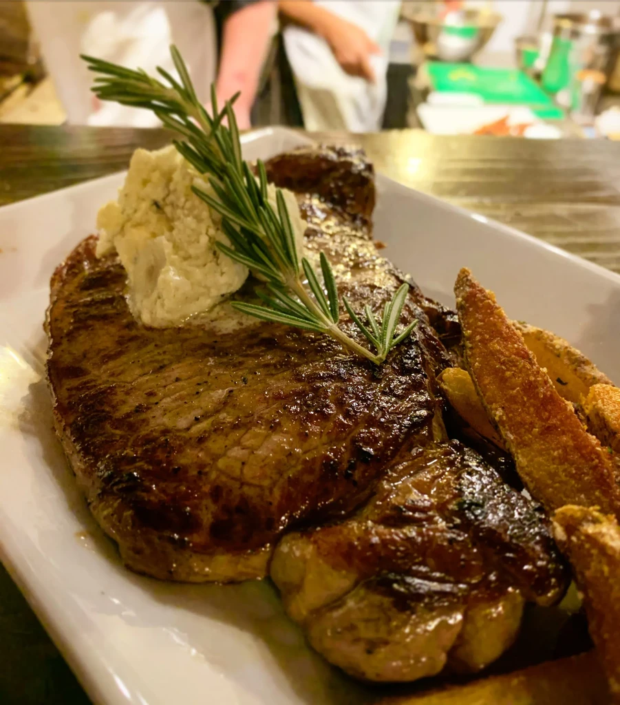Grilled steak with compound butter, rosemary, and wedge-cut fries.