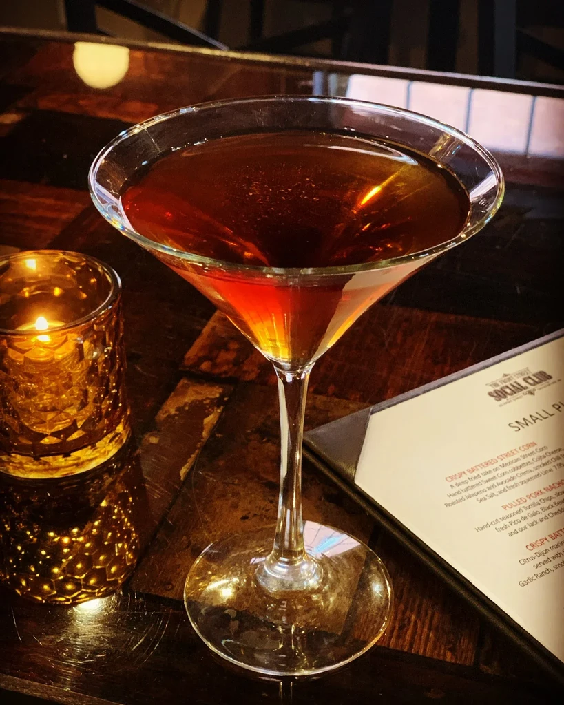 Amber cocktail, lit candle, and menu on a dark rustic table.