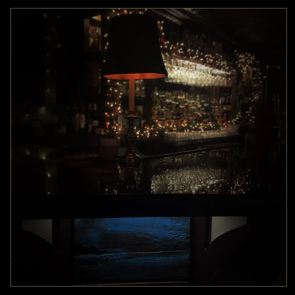 Ornate lamp glows on bar, with bottles and bokeh string lights.