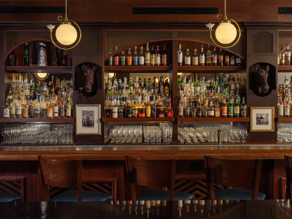 Classic wooden bar with bottled spirits, bar stools, and warm lighting.