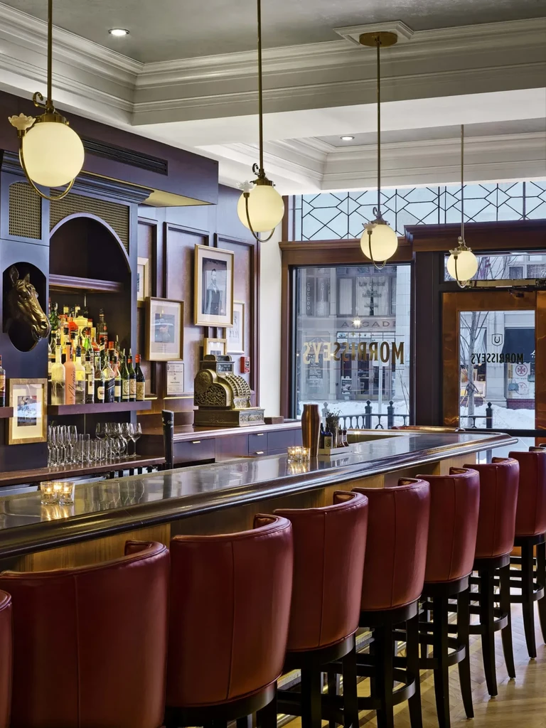Elegant dark wood bar with red stools, liquor, glassware, and street view.