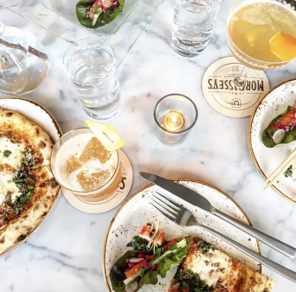 Overhead restaurant table with pizza, cocktails, salads, and a lit candle.