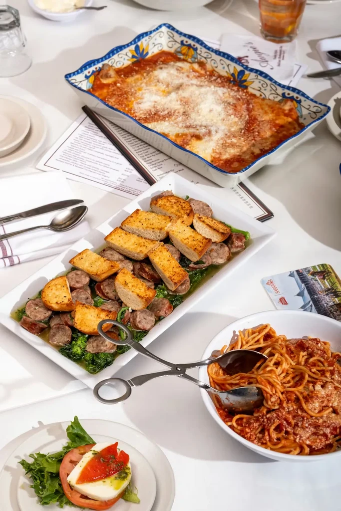 Overhead: Restaurant table with lasagna, spaghetti, sausage, Caprese salad.
