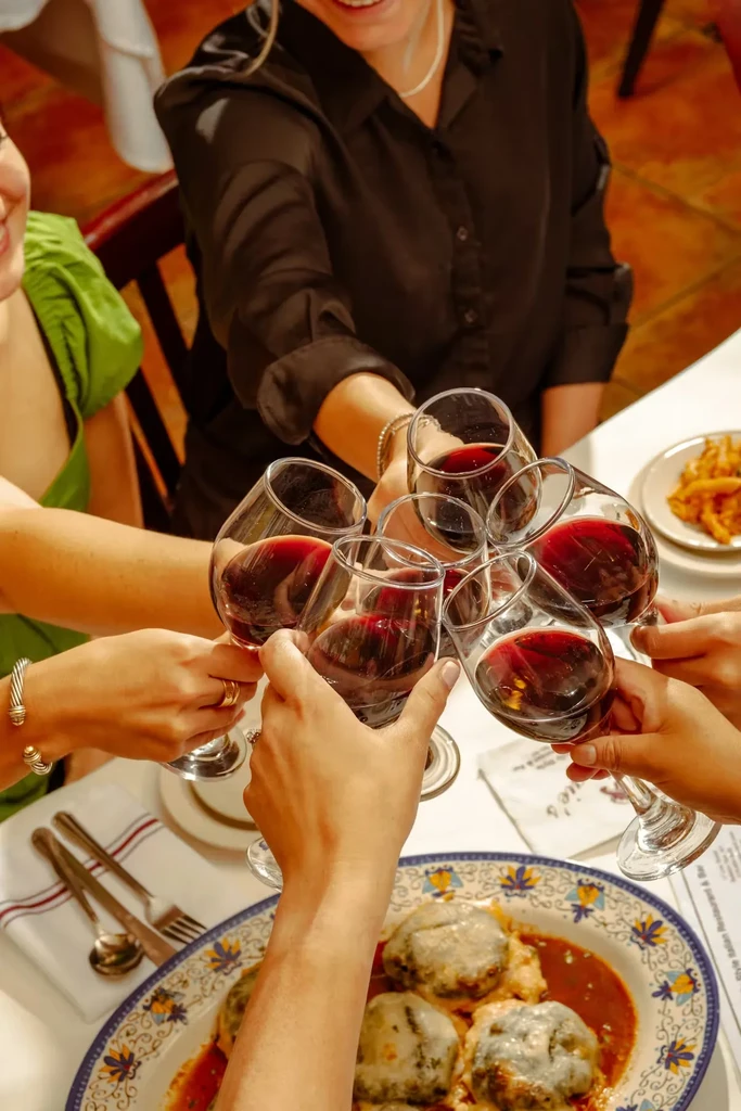 Group of people making a red wine toast over dinner.