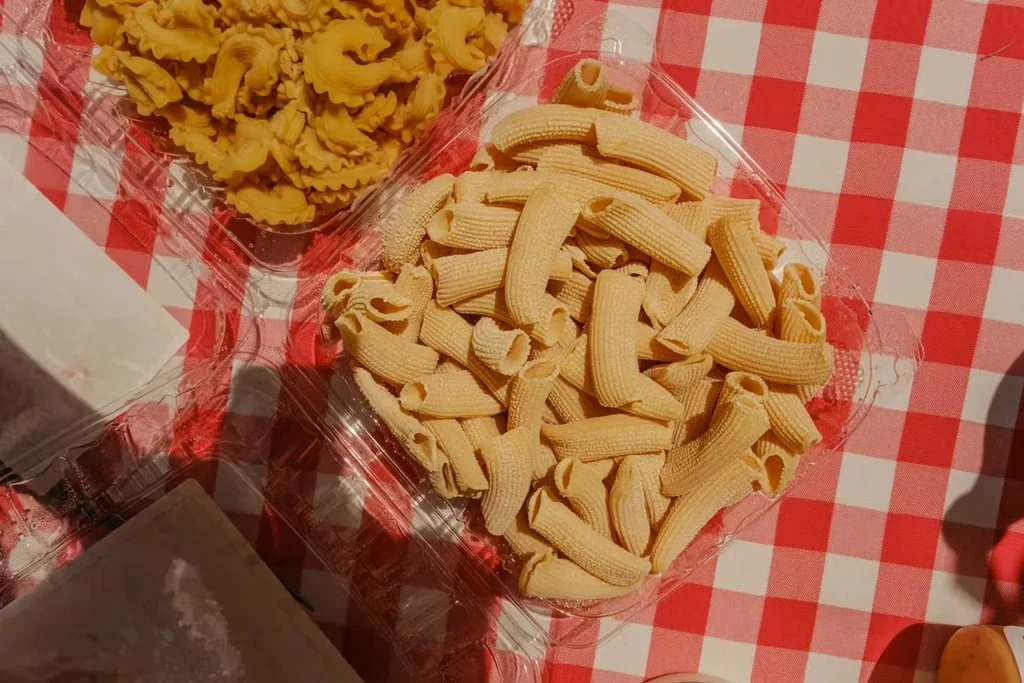 Overhead view of yellow uncooked pasta in containers on a checkered tablecloth.