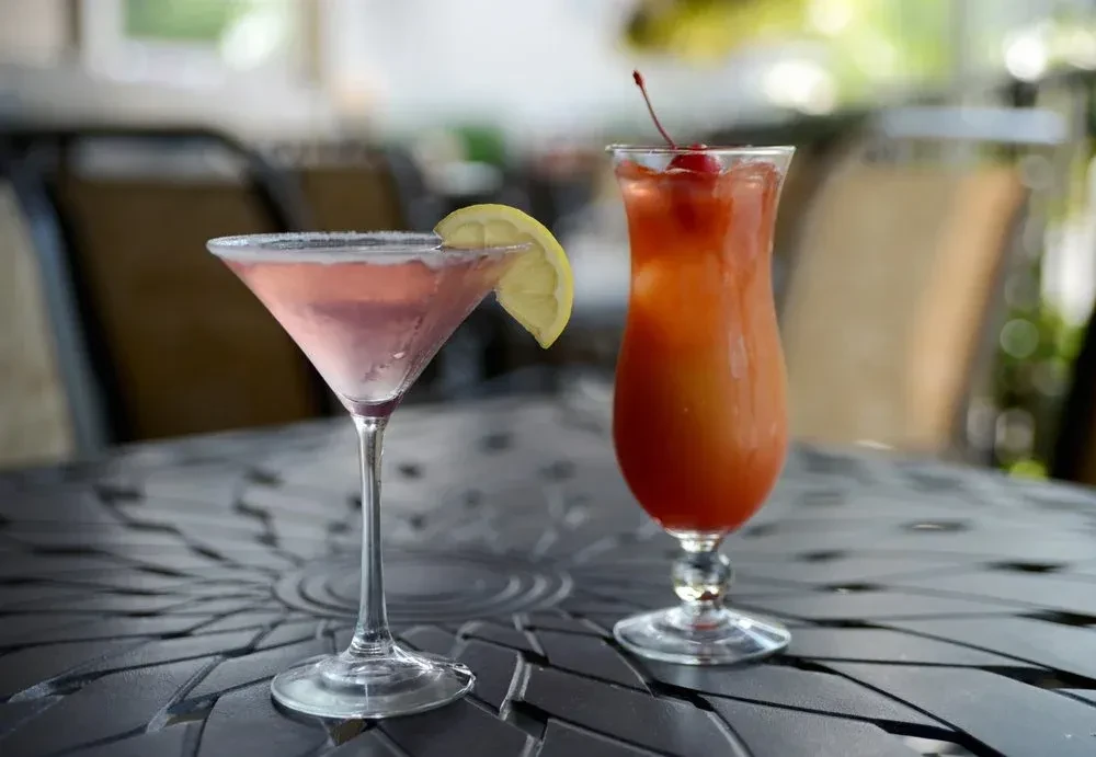 Pink martini and layered orange drink on a dark patio table.