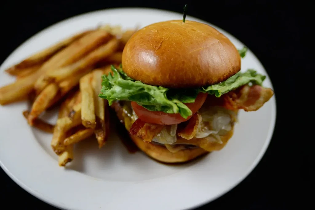 Gourmet burger, bacon, cheese, lettuce, and golden fries on a plate.