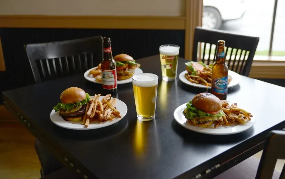 Three burgers with fries, two bottled, and two draft beers.