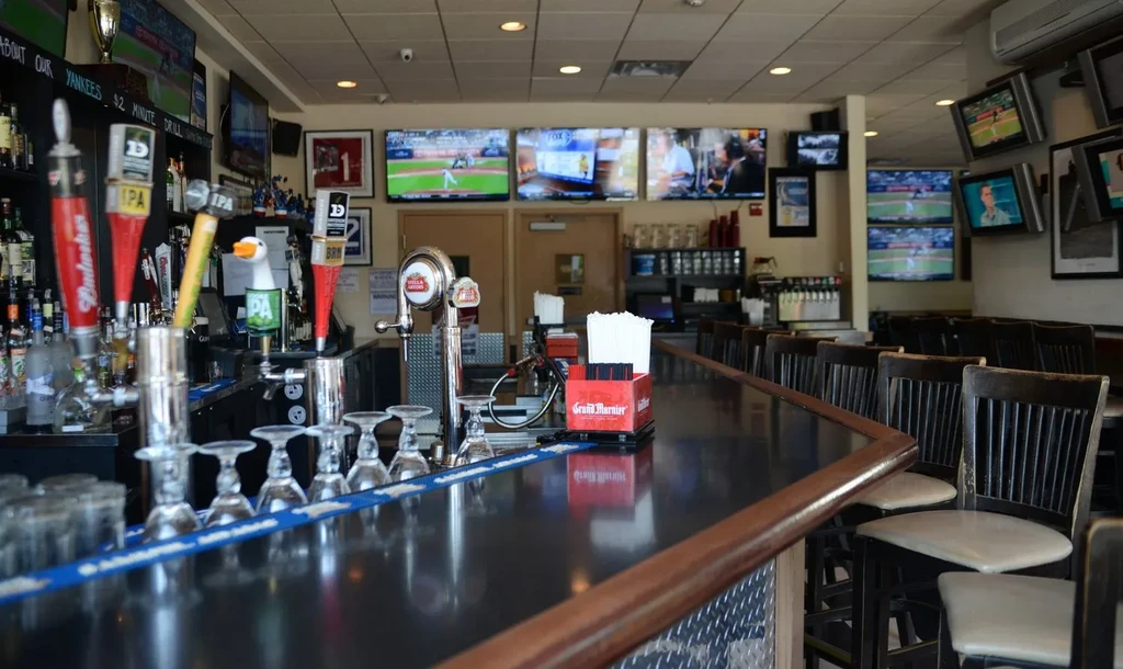 Empty sports bar with polished bar, beer taps, and sports TVs.