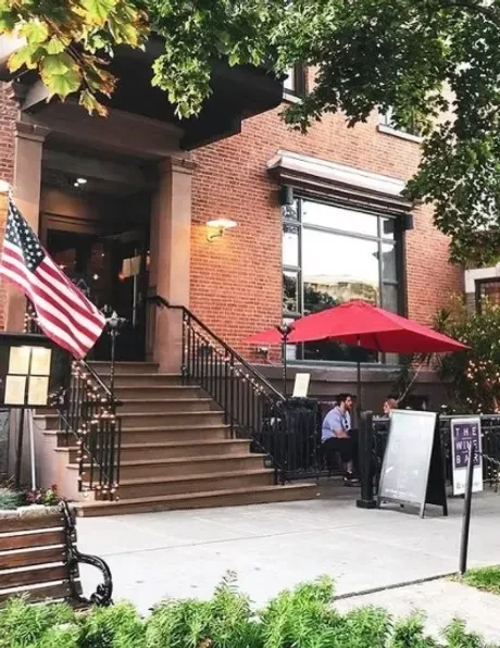 Brick wine bar, prominent steps, patio with two patrons, American flag.