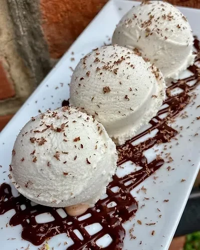 Three scoops of vanilla ice cream with chocolate shavings and drizzled sauce.