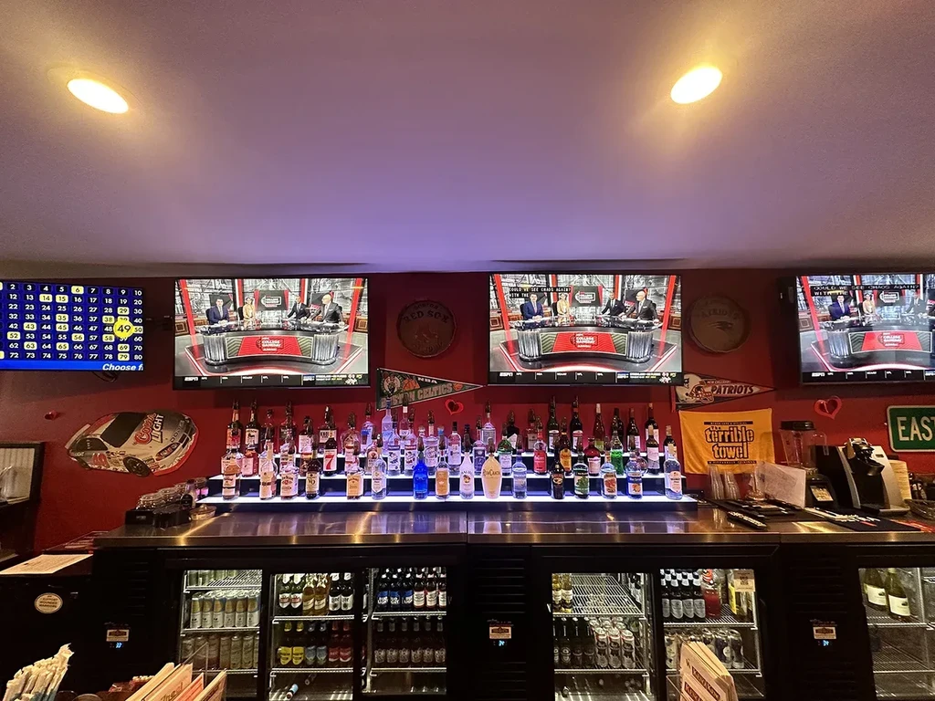 Vibrant sports bar with backlit liquor display, Boston sports memorabilia, and TVs.