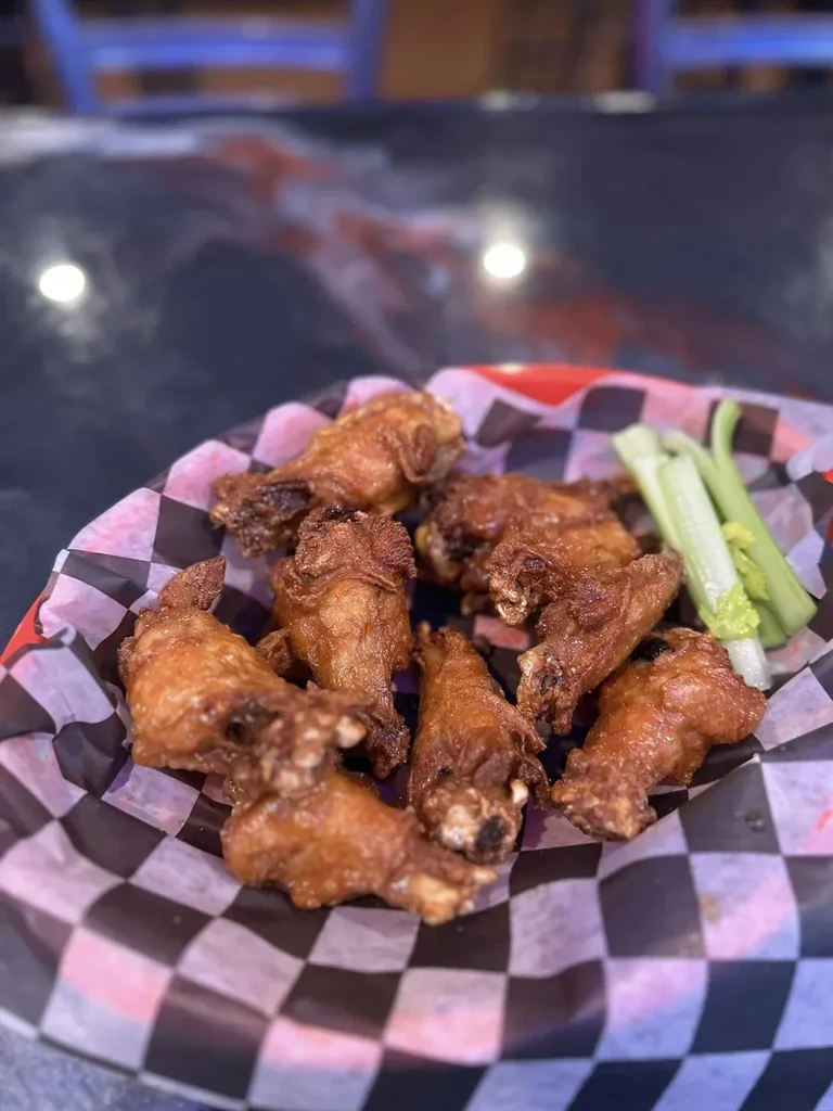 Crispy golden-brown chicken wings with celery in a red basket.