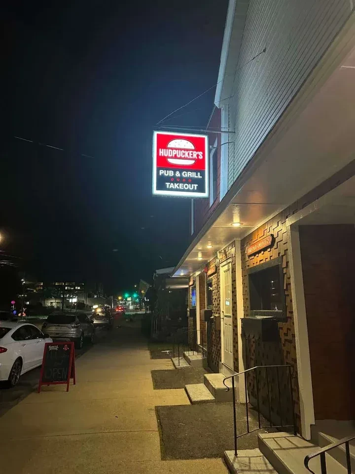 Nighttime exterior of Hudpucker's Pub & Grill Takeout with a bright red sign.