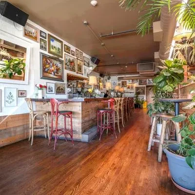 Eclectic bar interior with wooden bar, red stools, gallery wall, and plants.