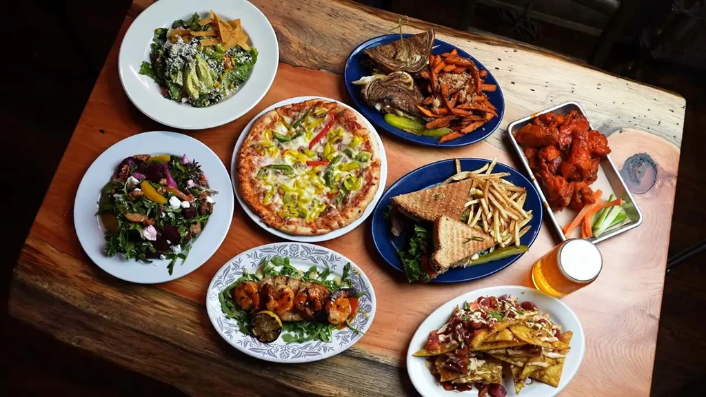 Rustic table with salads, wings, nachos, pizza, grilled food, and beer.