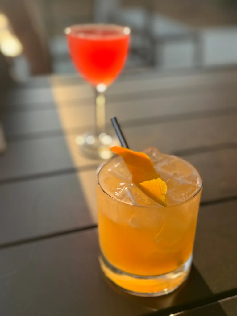 Two cocktails, orange and red, on a sunny outdoor table.