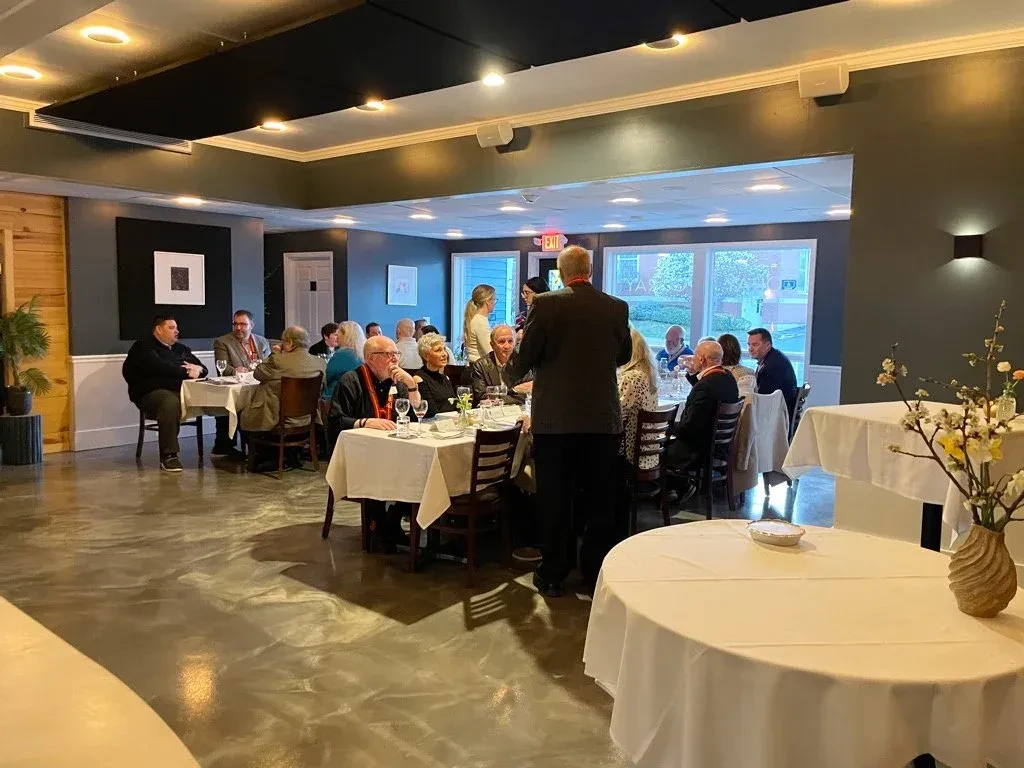 Warmly lit restaurant interior with people seated at white-clothed tables.