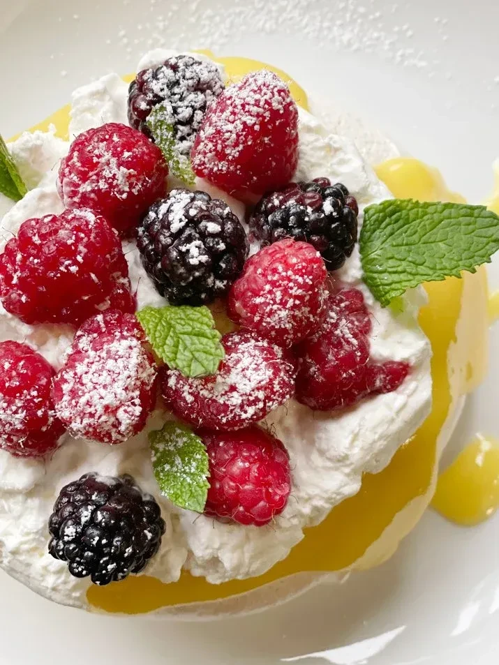 Pavlova with whipped cream, raspberries, blackberries, powdered sugar, mint, lemon sauce.