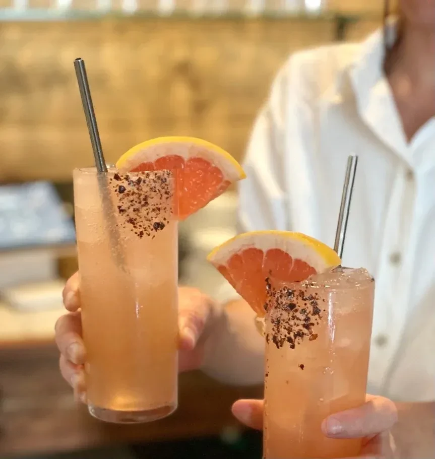 Two pink cocktails with grapefruit, spiced rims, and metal straws.
