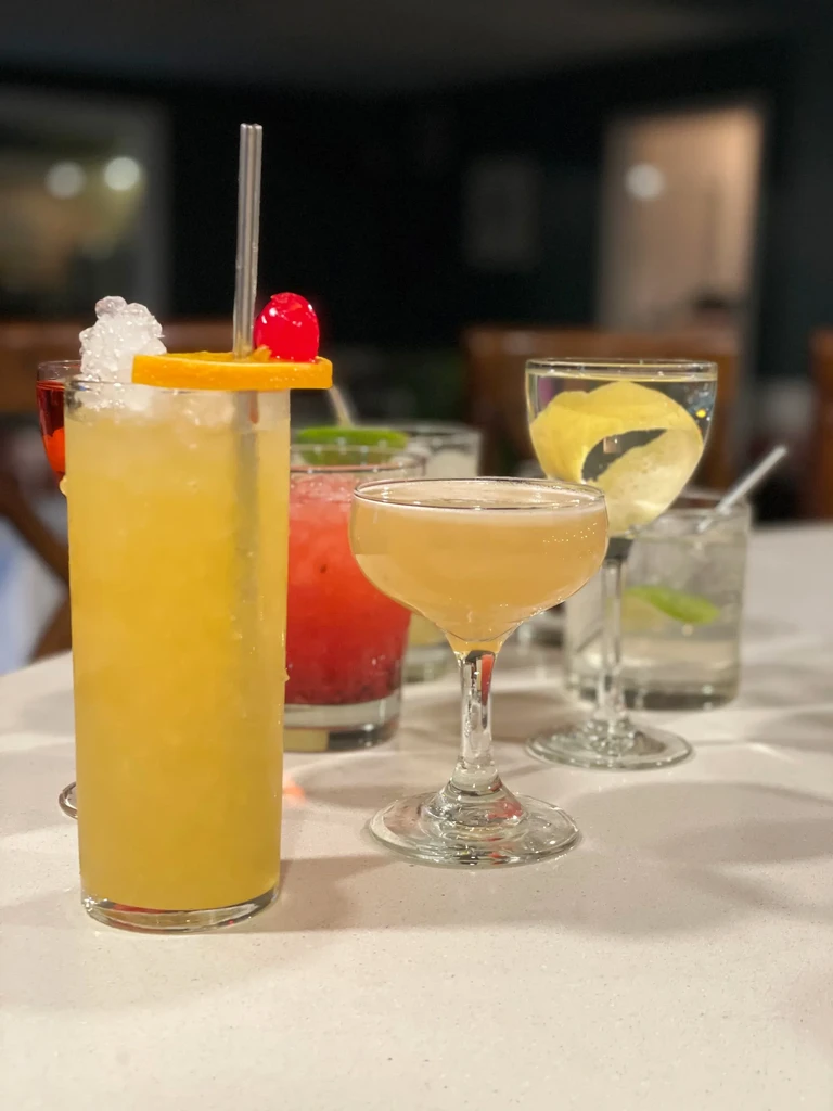 Garnished cocktails arranged on a light table in a dimly lit bar.