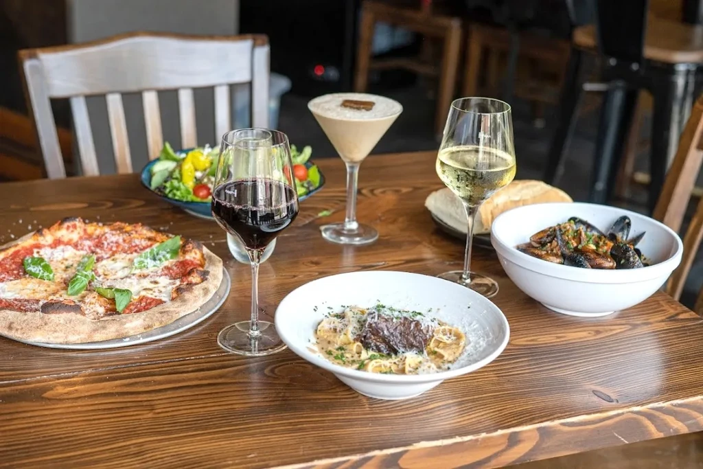 Restaurant table with pizza, pasta, salad, mussels, wine, and a cocktail.