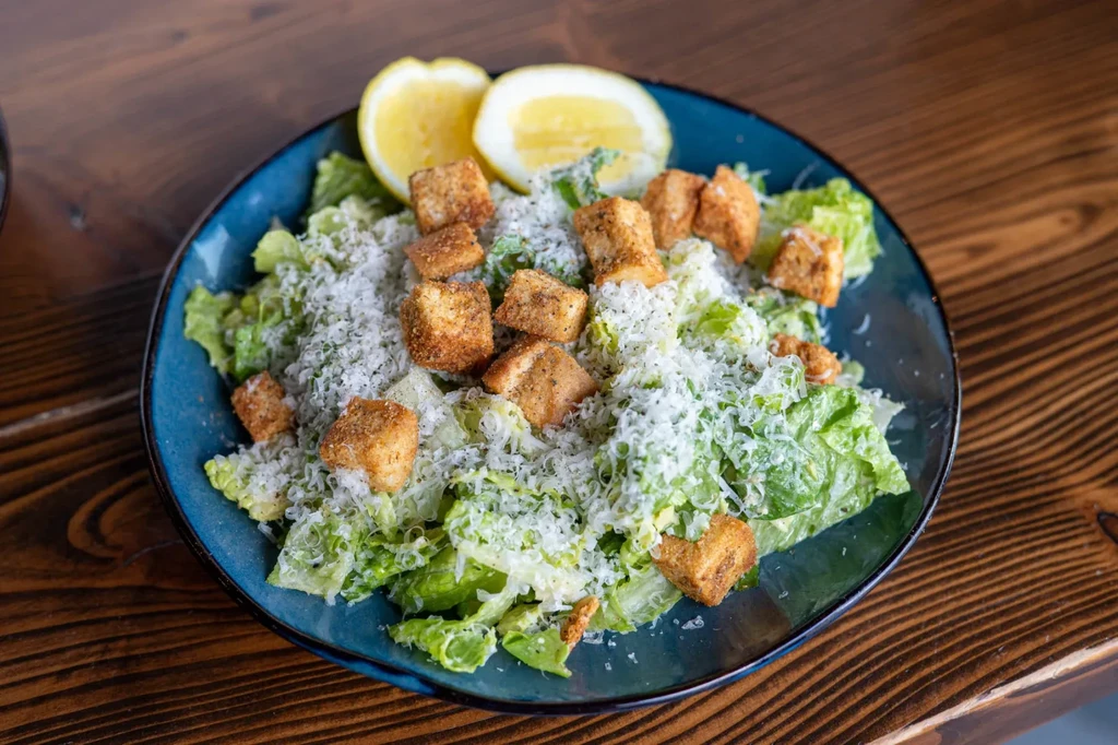 Caesar salad with Parmesan, croutons, and lemon slices on a teal plate.