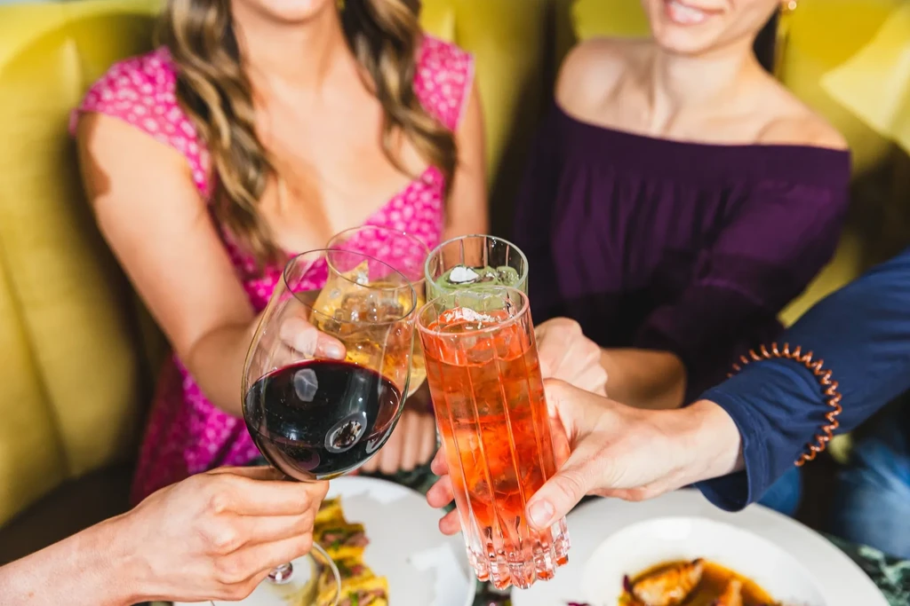 Close-up of four hands toasting with colorful drinks at a restaurant.