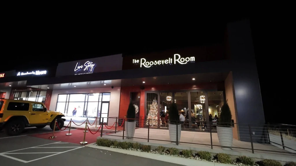 Illuminated Love Story and Roosevelt Room storefronts at night with a Jeep.