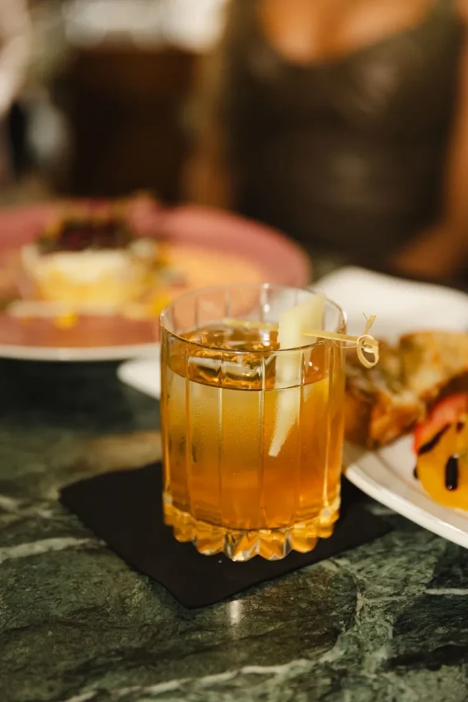Close-up of amber cocktail with fruit slice on green marble table.
