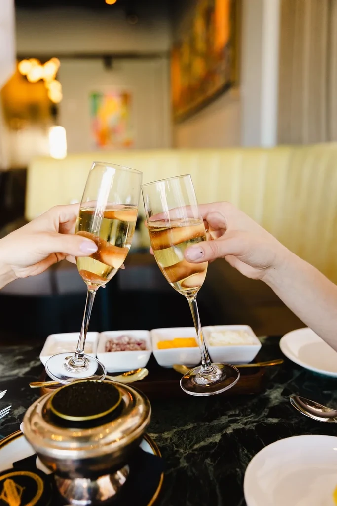 Hands clinking champagne flutes; upscale restaurant table with caviar.
