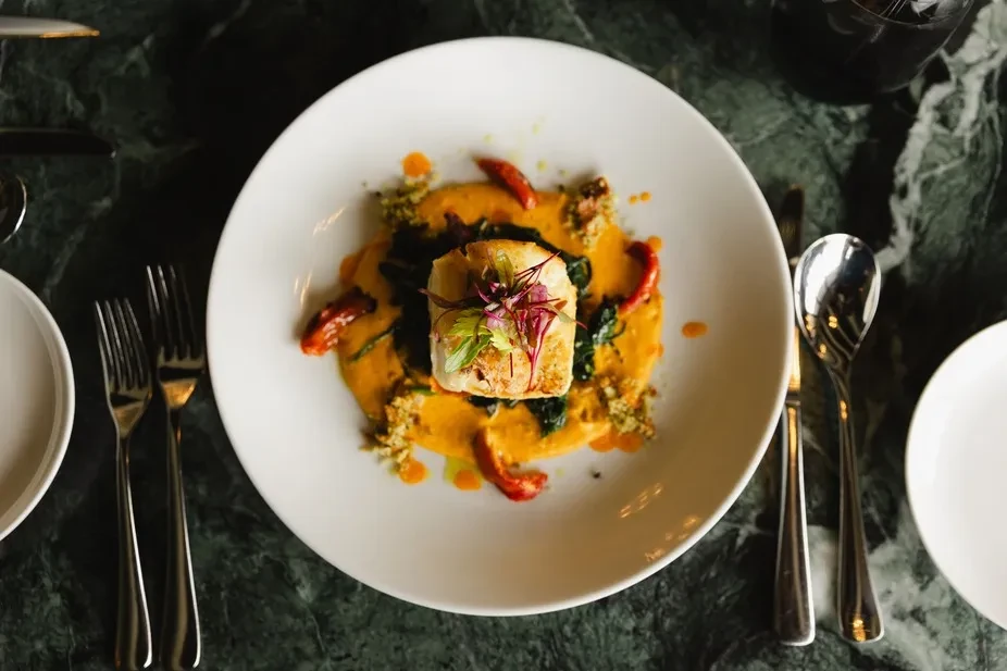 Meticulously plated white fish, microgreens, orange sauce, and roasted peppers.