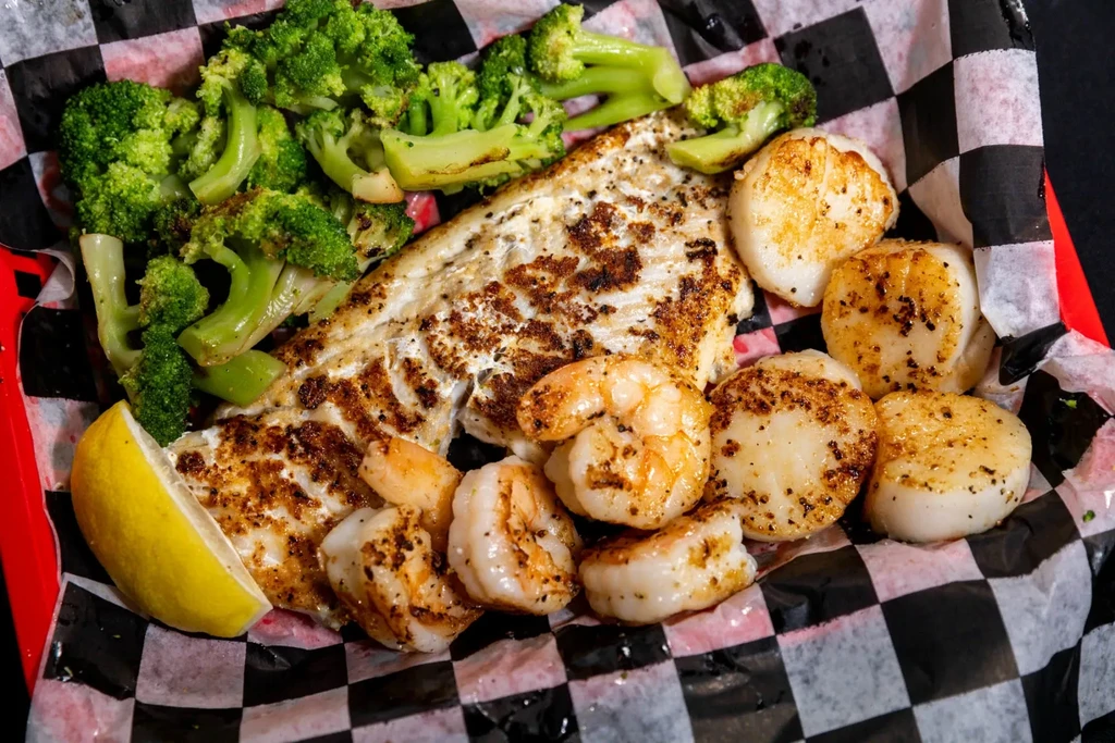 Seafood basket with grilled fish, shrimp, scallops, broccoli, and lemon.