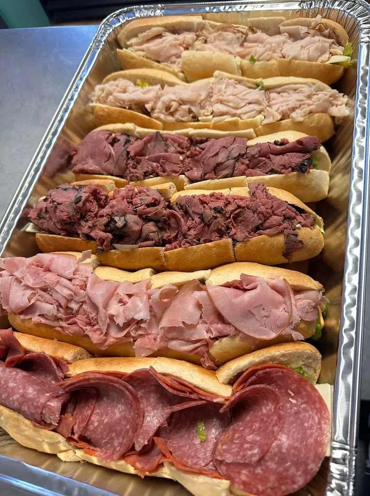 Catering tray with rows of turkey, roast beef, ham, and salami subs.