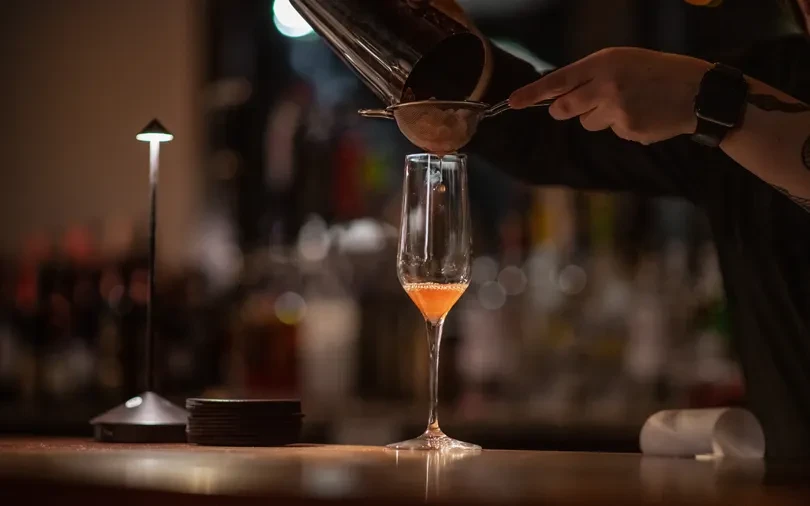Close-up: Bartender's hand straining a red cocktail into a champagne flute.