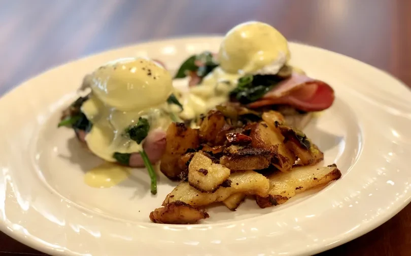 Top-down view: two Eggs Benedict with ham, spinach, and potatoes.