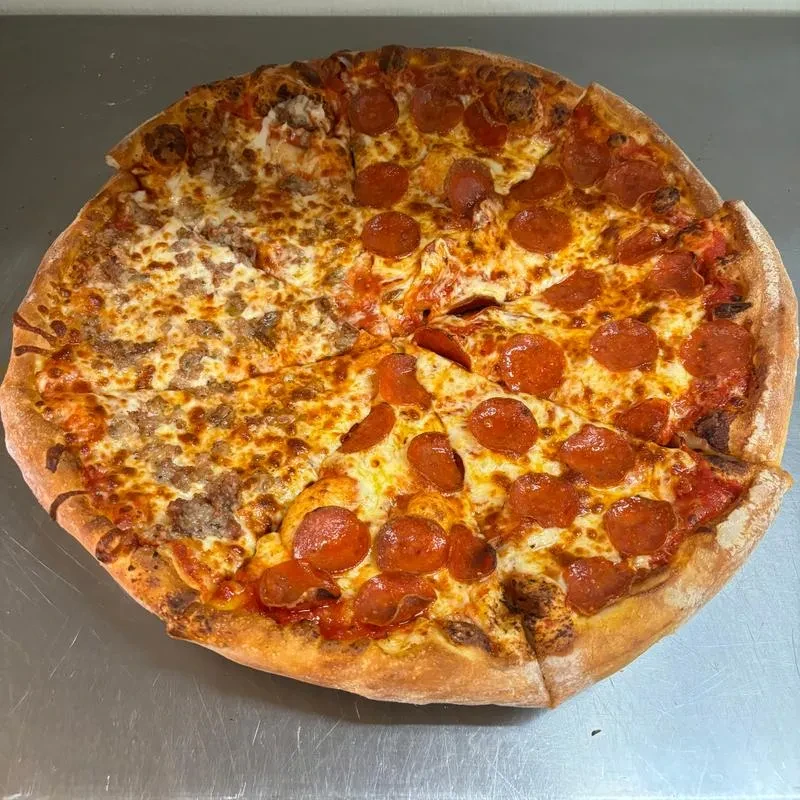 Sliced round pizza, half pepperoni, half sausage, on steel counter.