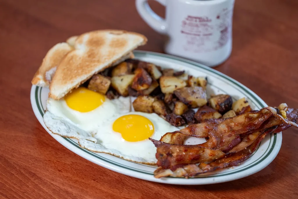 Hearty breakfast plate with sunny-side-up eggs, bacon, home fries, and toast.