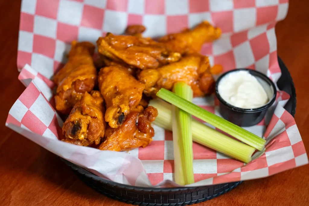 Buffalo chicken wings, celery, and white dipping sauce in a basket.