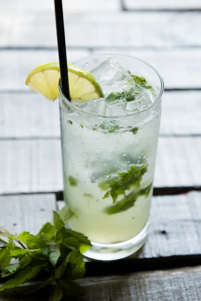 Mojito cocktail with mint, lime, ice, and straw on wood.