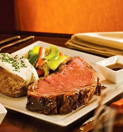 Plated medium-rare prime rib, baked potato, vegetables, and sauce.