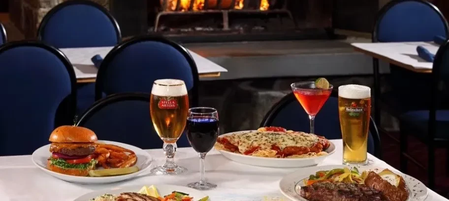 Restaurant table laden with various dishes and drinks, fireplace in background.