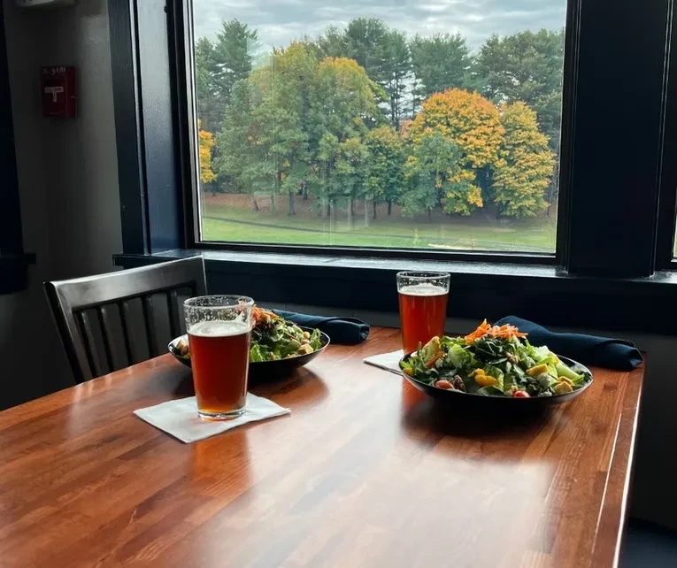 Restaurant table with salads, beers, overlooking an autumn landscape.