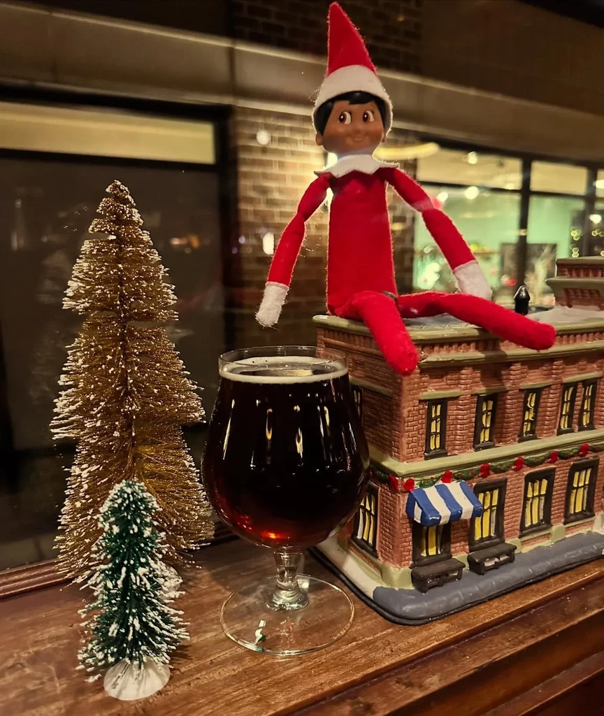 Dark beer, brown Elf on Shelf, and festive mini trees on wood.