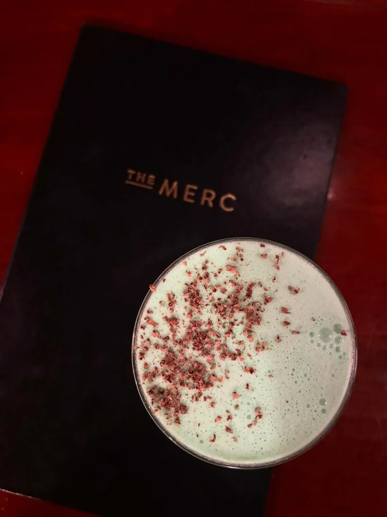 Mint green martini with red sprinkles next to 'THE MERC' menu.