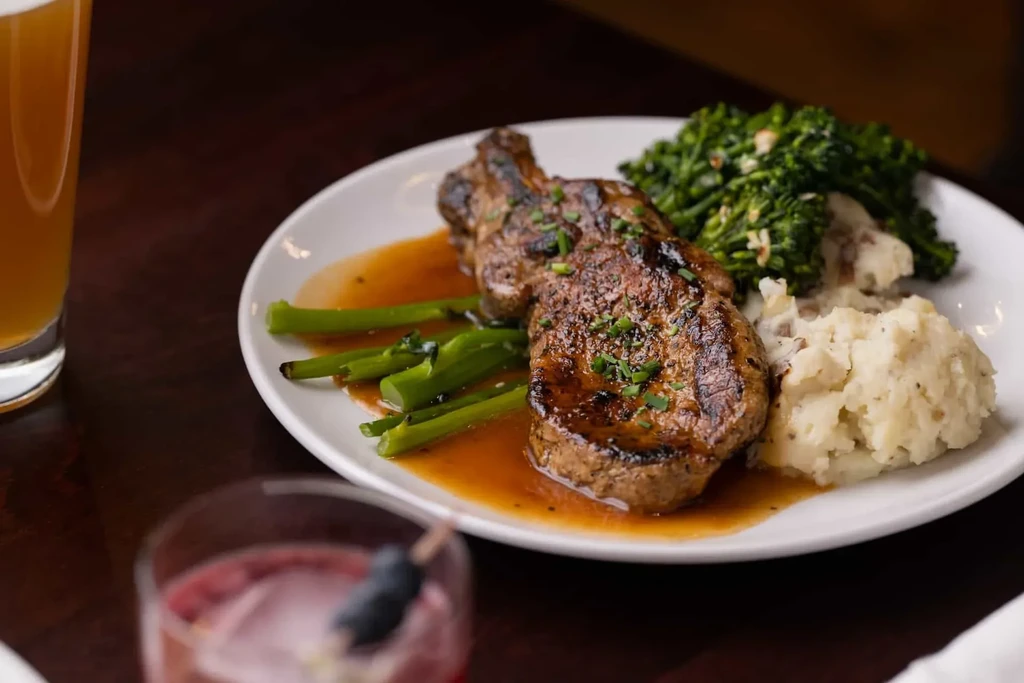 Grilled meat, mashed potatoes, asparagus, and broccolini plated with sauce.