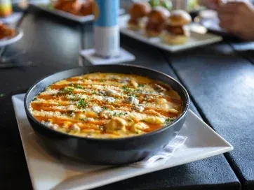Bowl of macaroni and cheese with shredded cheese, orange sauce, and herbs.
